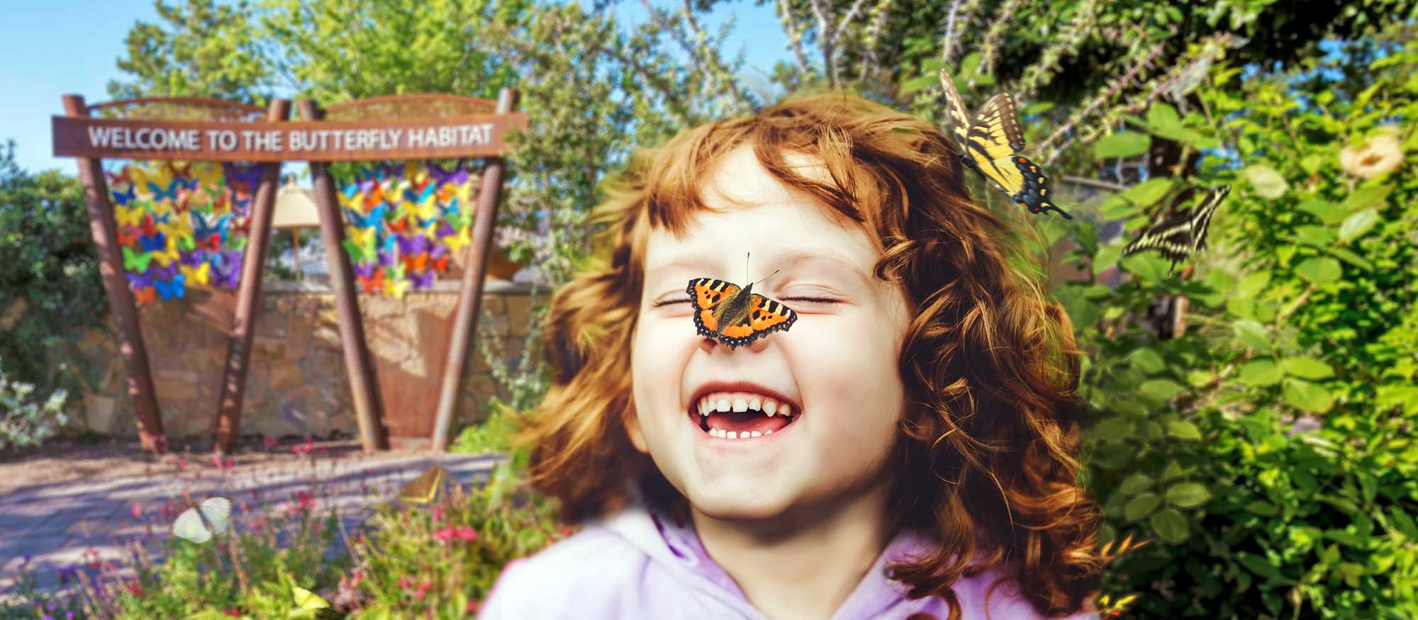 A joyful child with closed eyes and a wide smile has a butterfly on their cheek. In the background, there's a colorful sign that reads 'Welcome to the Butterfly Habitat' amidst lush greenery.