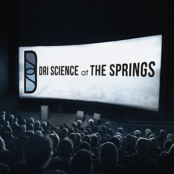 Theater audience depicted viewing a large wide theater screen with the words DRI Science at the Springs