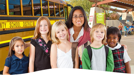 Group of students with their teacher standing in front of a school bus, smiling.