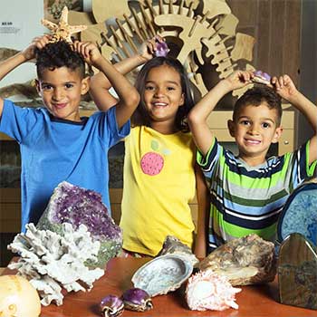 Three smiling children posing with fossils and gems inside the Nature Exchange