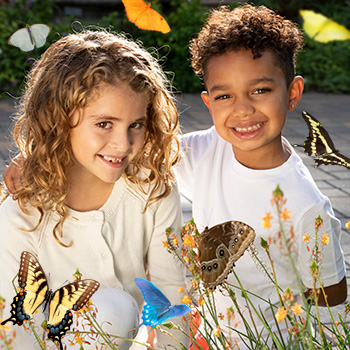 Two children surrounded by colorful butterflies inside the Butterfly Habitat
