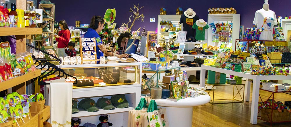 Interior of a vibrant gift shop with various items on display including hats, bags, and clothing. Shoppers are browsing the products.