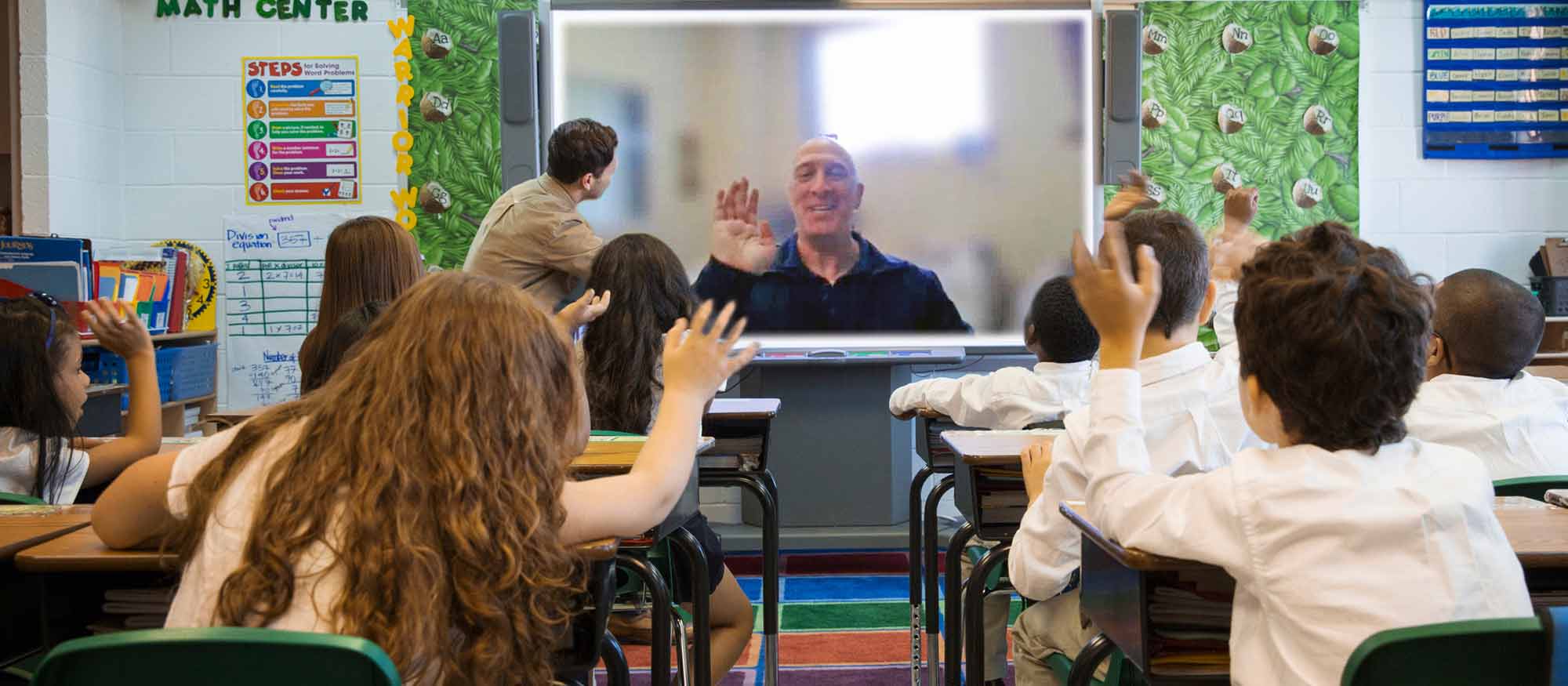 A classroom full of students interacting with Springs Preserve program expert who appears on a large screen via video call. The room is decorated with educational posters.